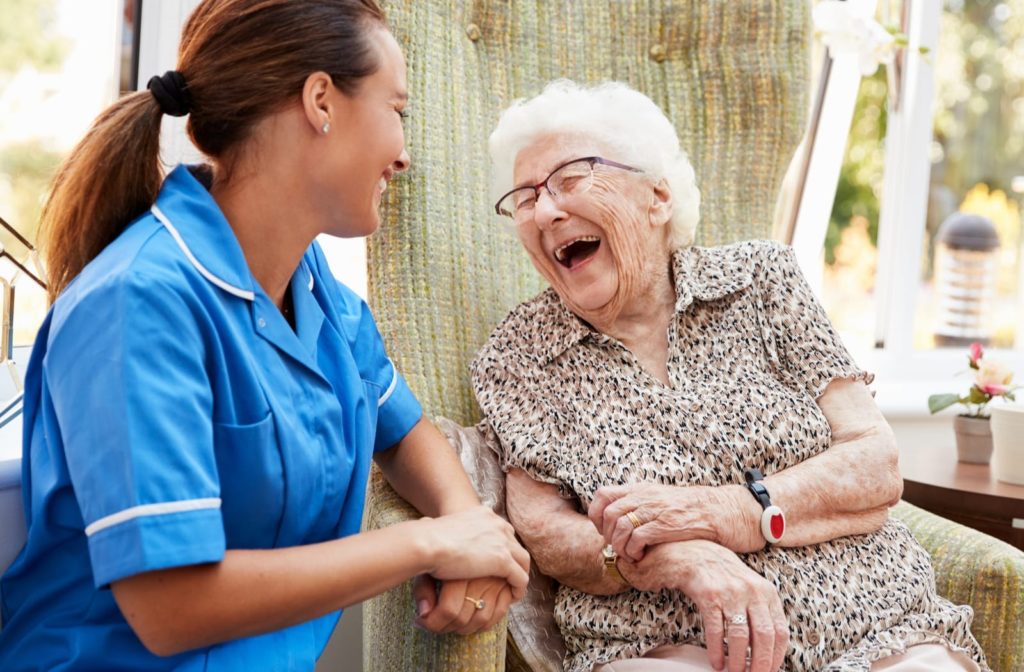 A senior woman shares a big laugh with a friendly staffer at a long-term care facility