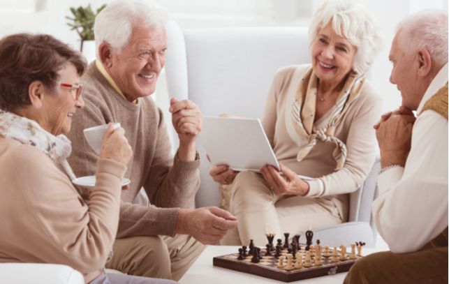 Happy seniors sitting in living room playing chess and socializing with one another