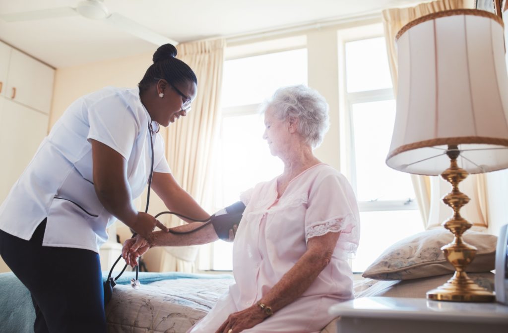 An assisted living nurse checking the blood pressure of an older adult woman in her bedroom.