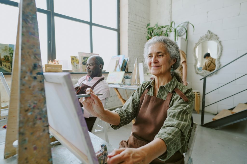 Older woman and man painting on canvases with brown smocks.