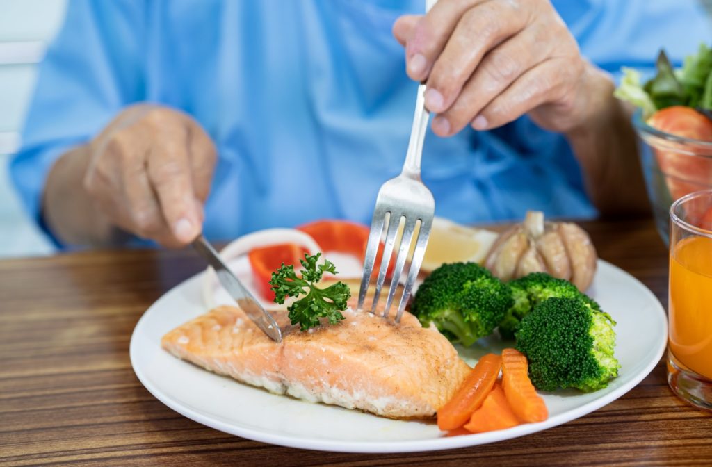 Close-up of a plate of vegetables with a large piece of salmon as someone digs into an anti-inflammatory meal.