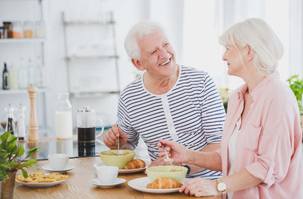 A senior couple smile at each other over breakfast, enjoying eating without experiencing any discomfort from their dentures