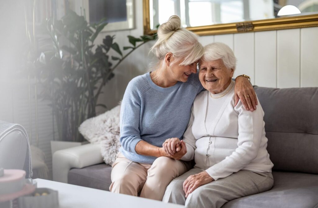 An adult holds their older parent in a loving embrace while sitting on the couch after a stay in respite care