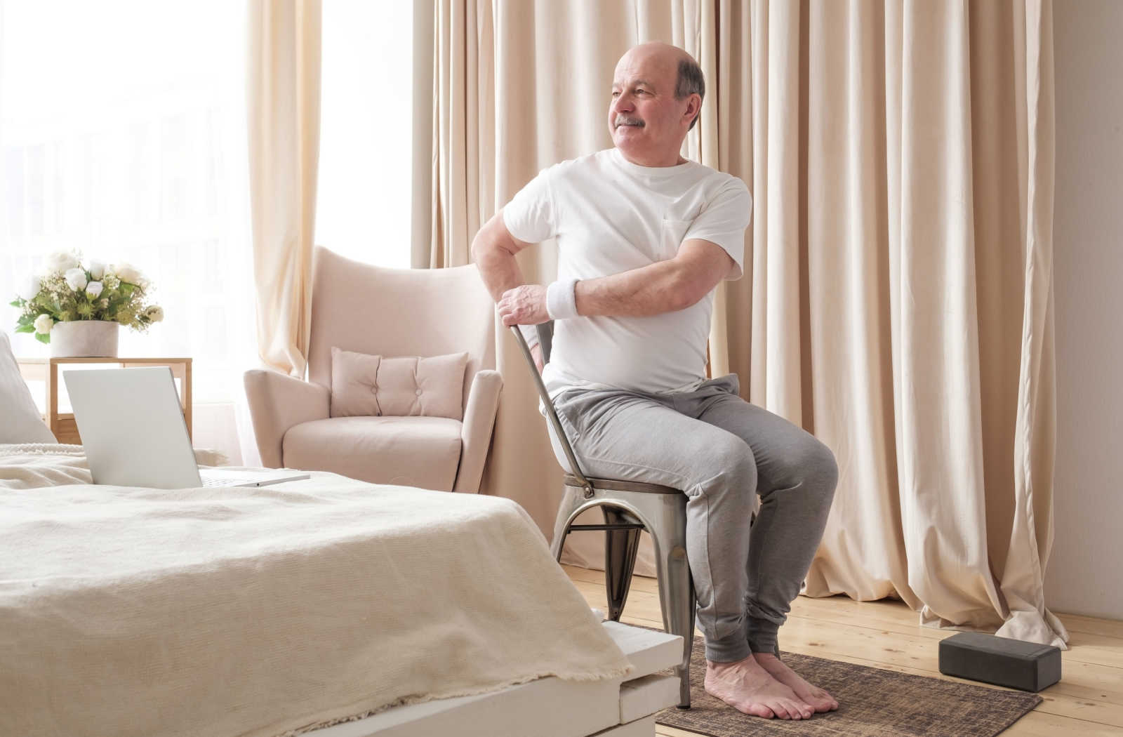 A senior man sitting up straight on a chair doing a posture exercise.