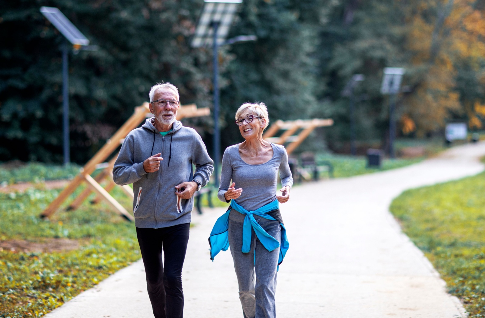 Two older adults smiling and walking on a path outdoors.