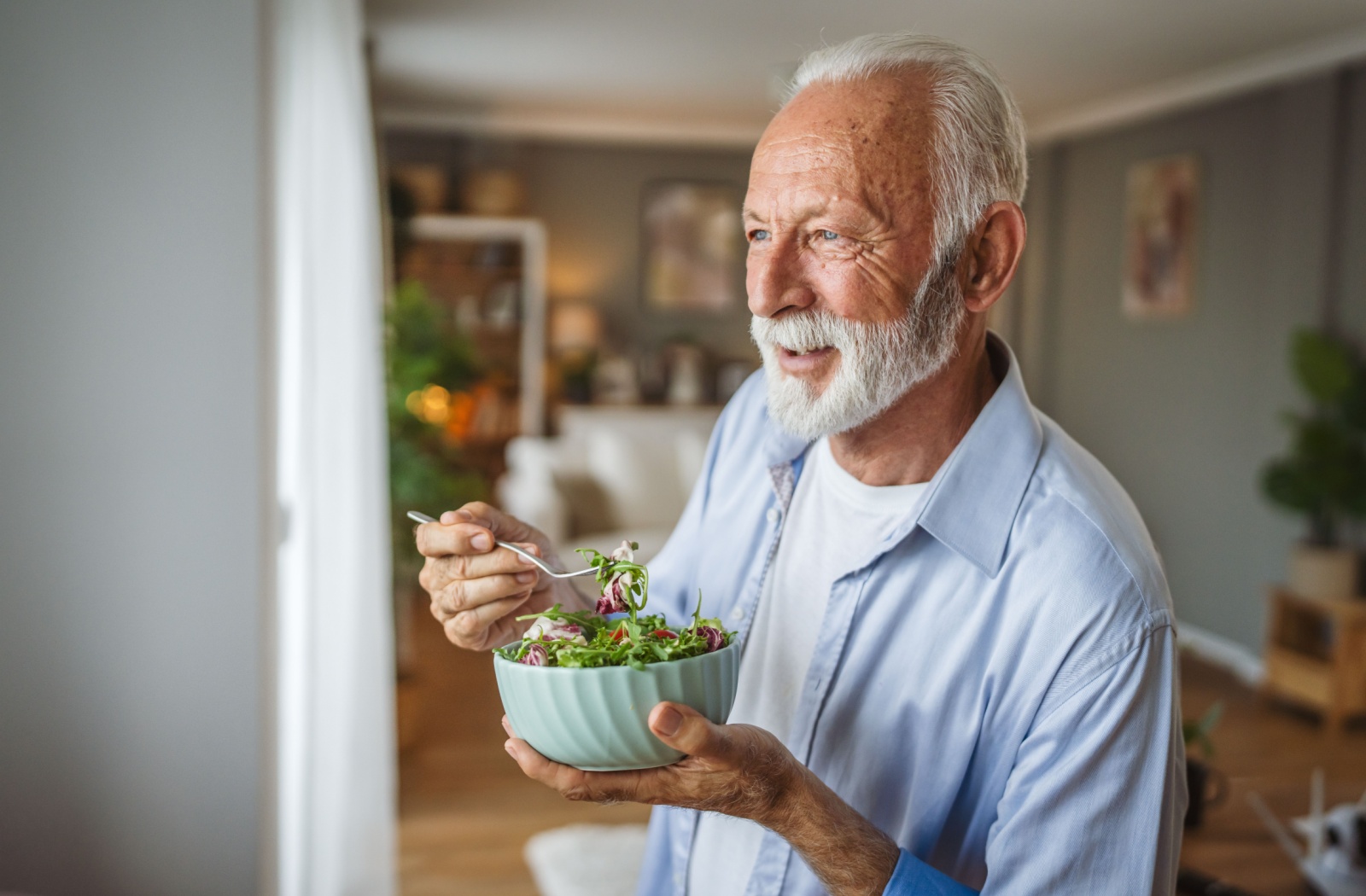 An older adult standing in their room in an assisted living community, enjoying a salad with nuts for an anti-inflammatory diet.