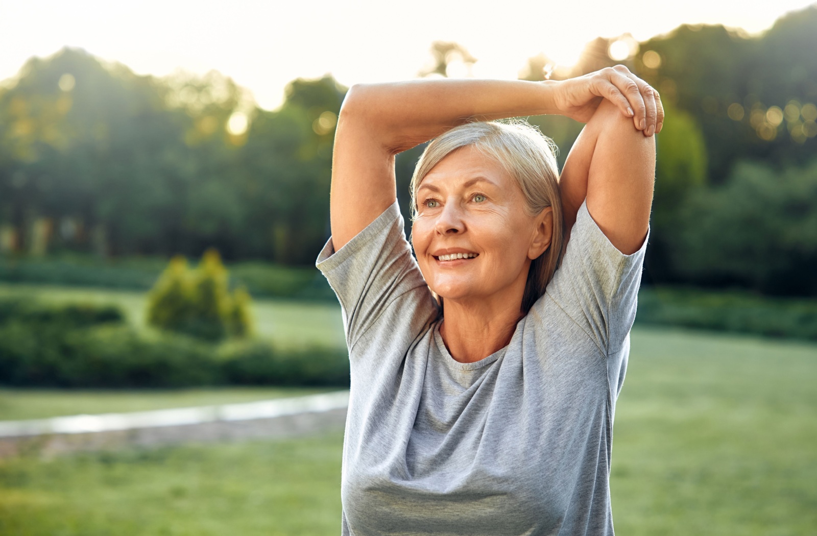 A senior stretching their shoulder outdoors to improve flexibility.
