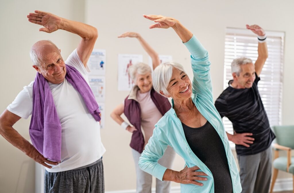 Seniors participating in a fitness class, stretching to improve flexibility in an assisted living setting.