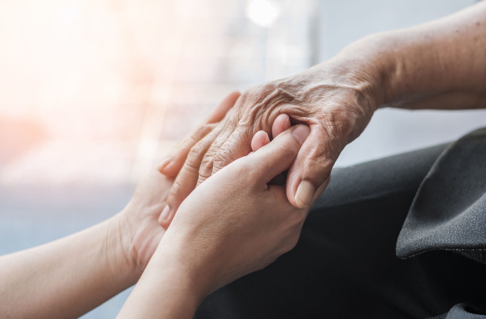 Younger hands gently holding older hands during a supportive conversation about a dementia diagnosis.