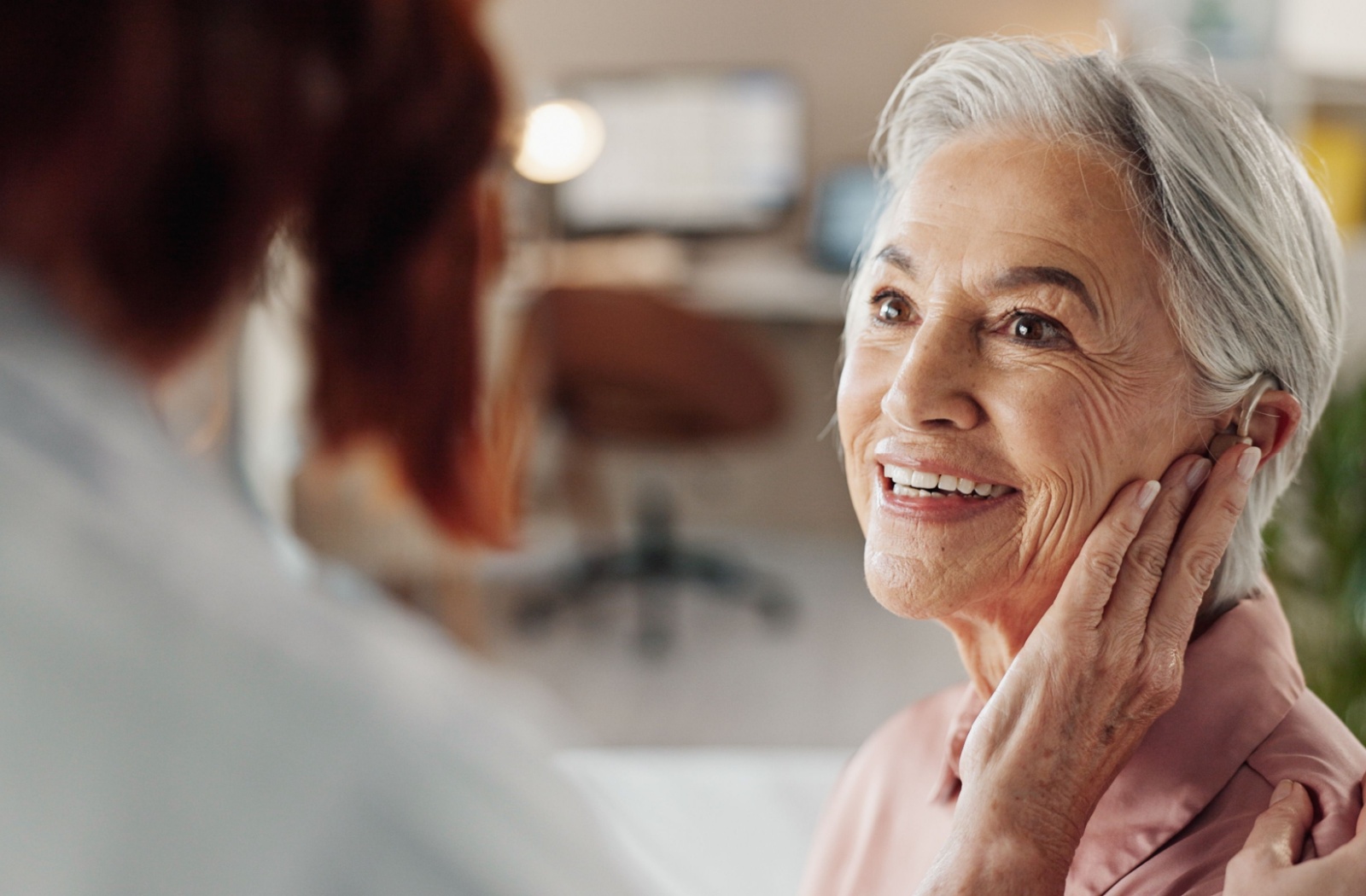 An older adult smiling with joy while trying out their new hearing aid.
