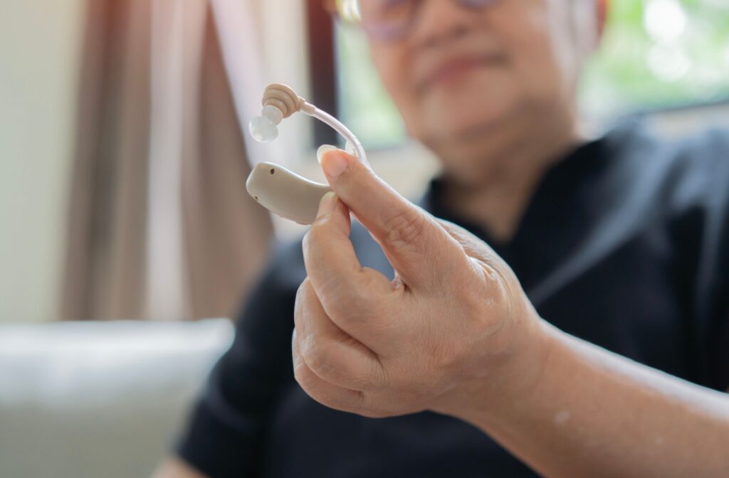An older adult holding up their newest hearing aid and smiling.