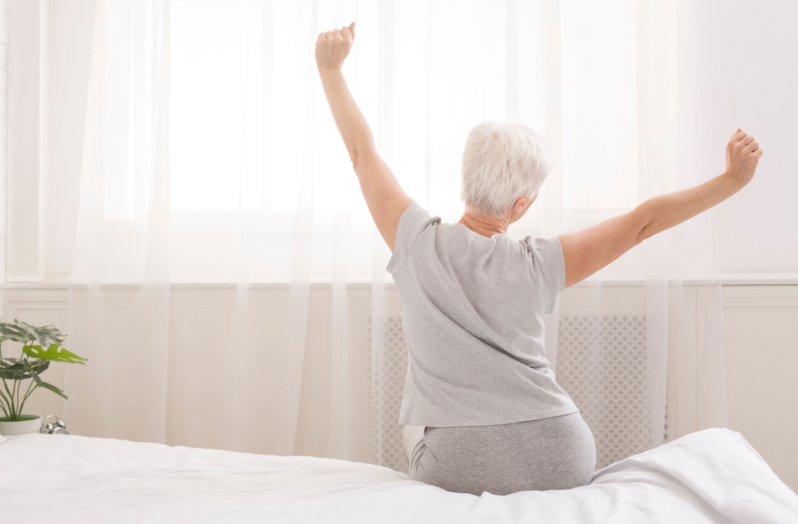 An older adult stretching in their sunlit bedroom after a good night's sleep.