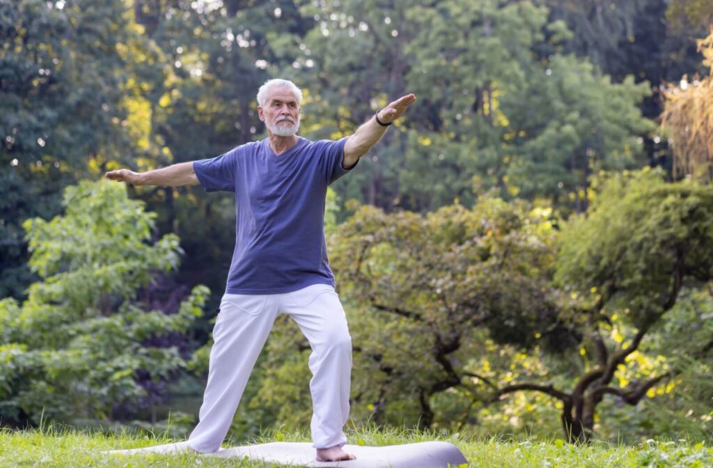 A senior in loose-fitting clothes practices tai chi poses while enjoying outdoor greenery, fresh air, and the sunshine