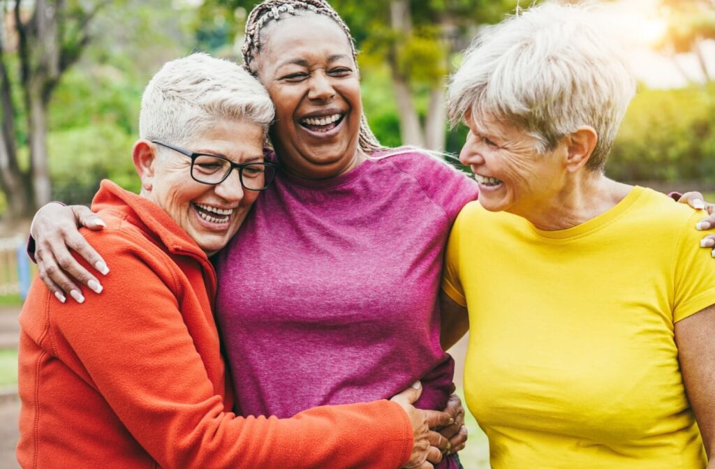 Group of seniors laughing and hugging outdoors showing friendship and connection in assisted living community