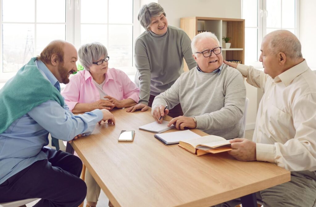 Seniors gathered at a table sharing conversation and activities in a bright assisted living community space